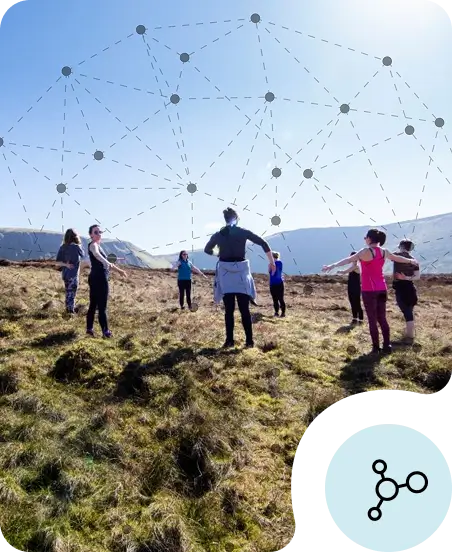 A group of people stand in a circle on grassy hills under a blue sky, stretching with arms out to promote wellbeing. A digital network pattern is superimposed in the sky; an icon with connecting nodes appears in the bottom right corner.