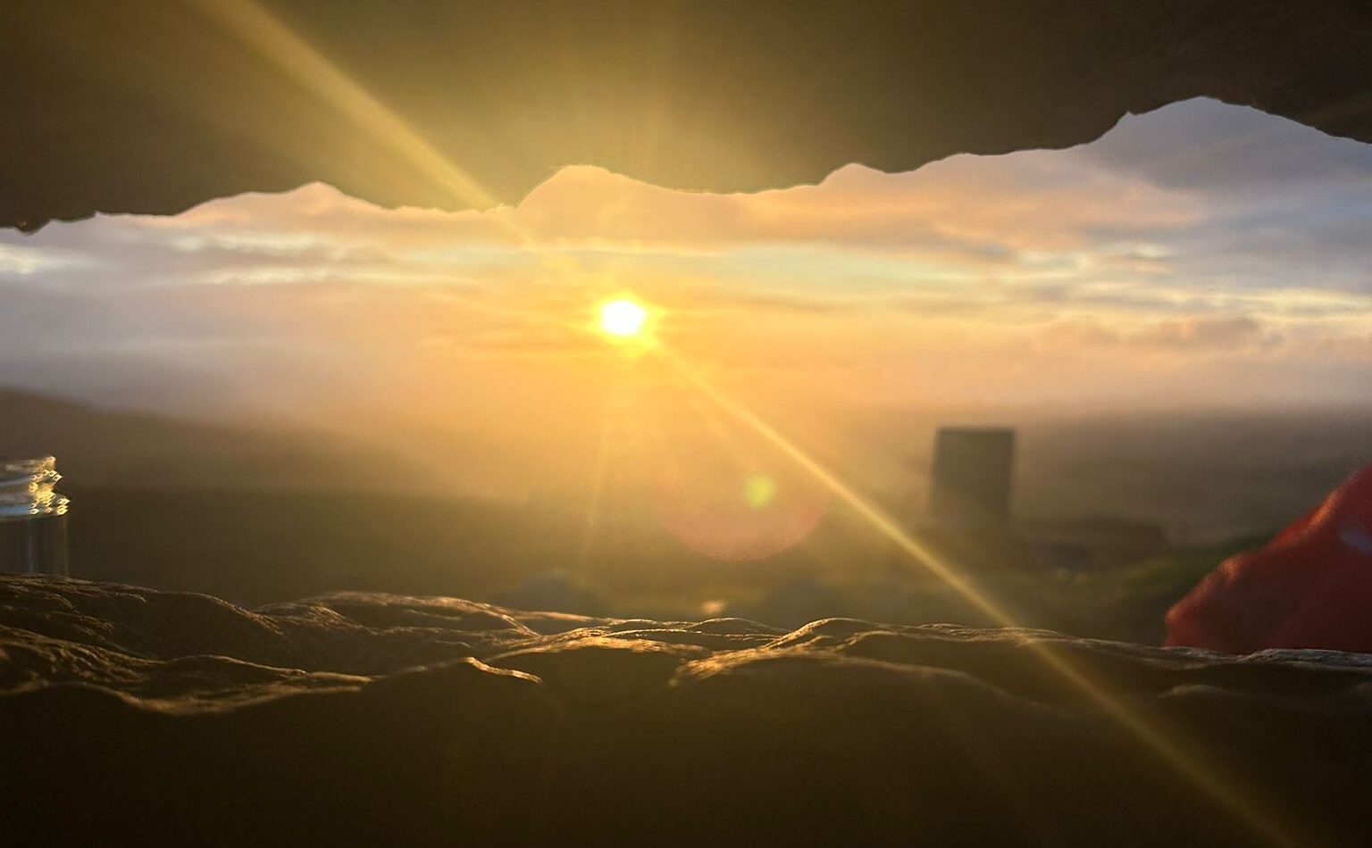 Golden sunlight streams through the light box opening of Cairn G at Carrowkeel, illuminating the ancient stone chamber at sunset. The warm rays create a dramatic beam of light across the stone floor, highlighting the alignment between the passage tomb and the horizon beyond.