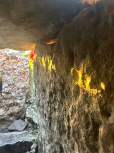Sunlight shines through a narrow opening in the stone structure of the Carrowkeel passage tomb, casting a warm golden glow across the weathered rock surface. The close-up view highlights the texture of the ancient stones and the dramatic effect of light entering the chamber during a seasonal alignment.