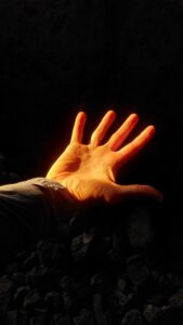 A hand reaches into a beam of golden sunlight inside the dark chamber of a Carrowkeel passage tomb. The warm light illuminates the palm and fingers against the shadowy stone interior, capturing the striking contrast between darkness and the seasonal sunlight entering the ancient monument.